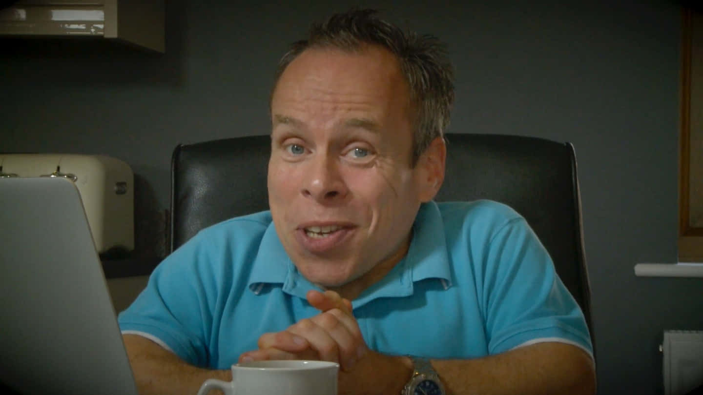 Warwick Davis Posing In A Dark Suit Background