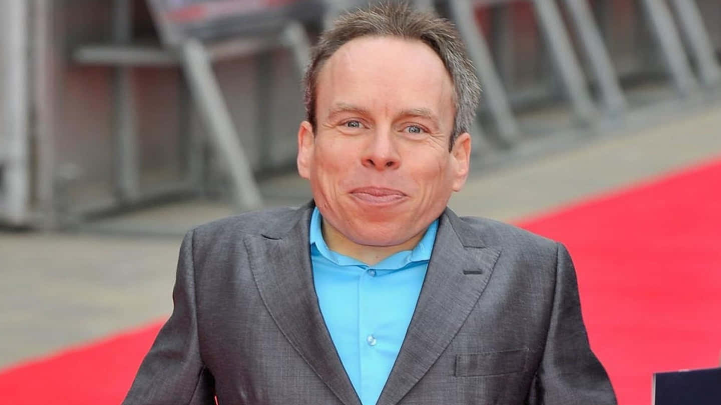 Warwick Davis Smiling During A Public Appearance Background