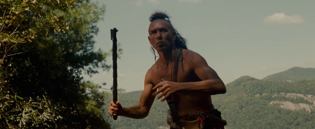 Wes Studi Native American Character Running With Tomahawk Background