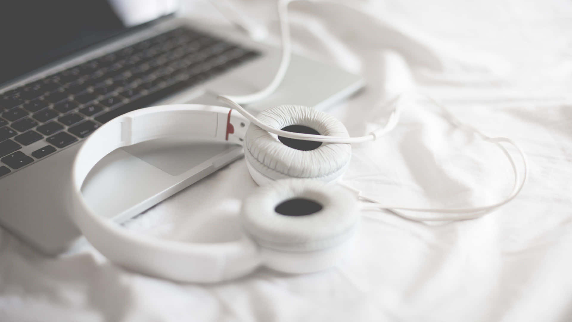 White Headphones On A Bed Next To A Laptop Background
