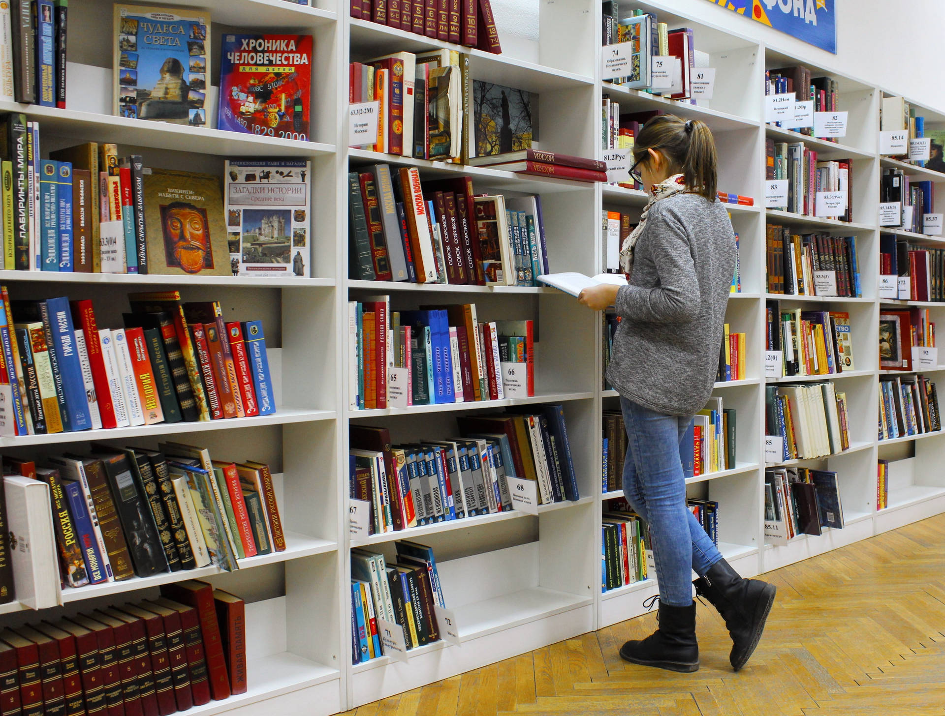 Woman Reading Reference Book Near Shelf