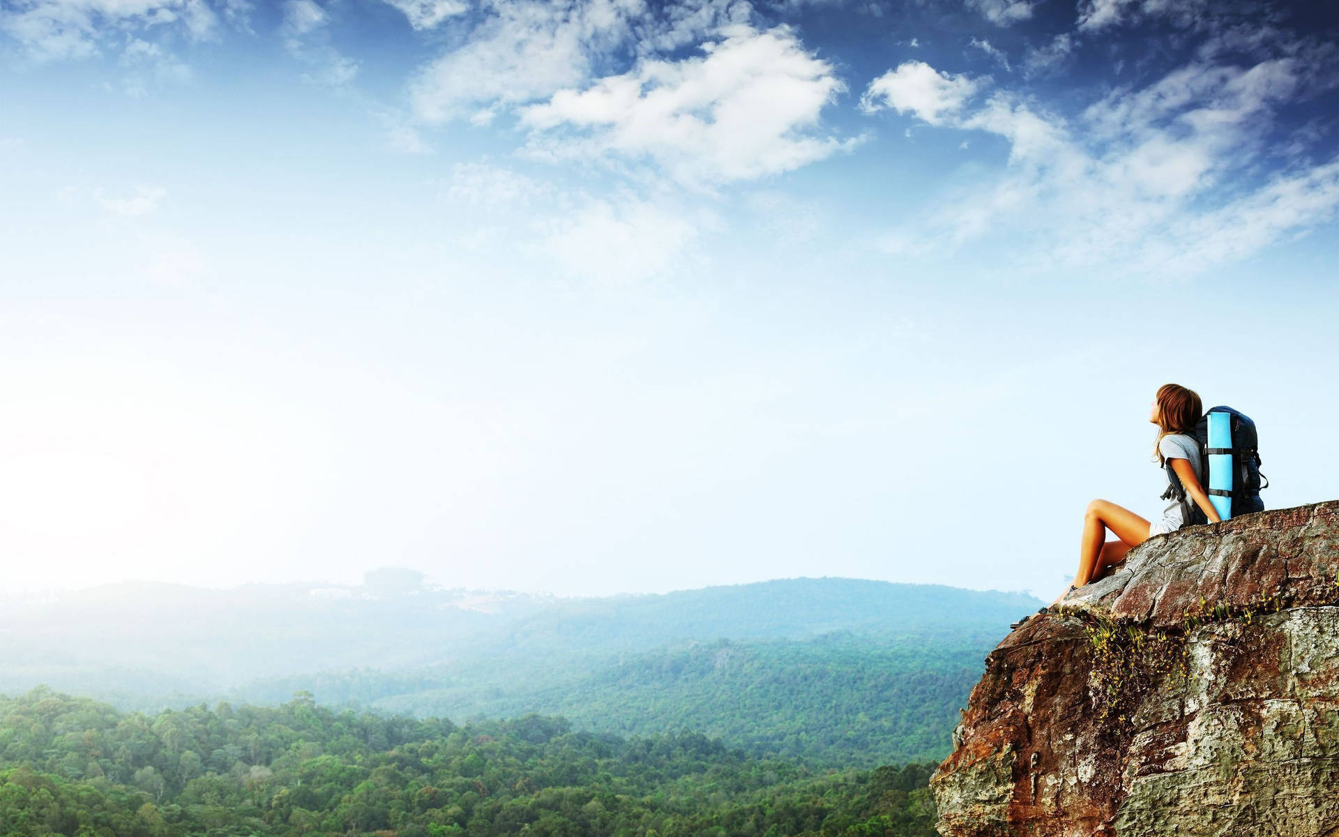 Woman Sitting On A Cliff Overlooking A Mountain Background