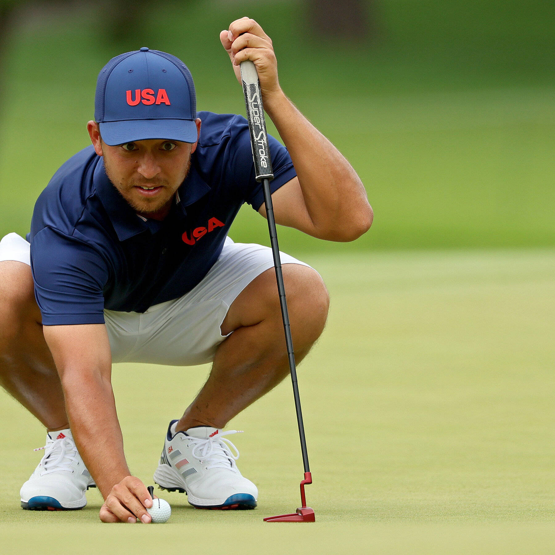 Xander Schauffele Crouching On Golf Course Background