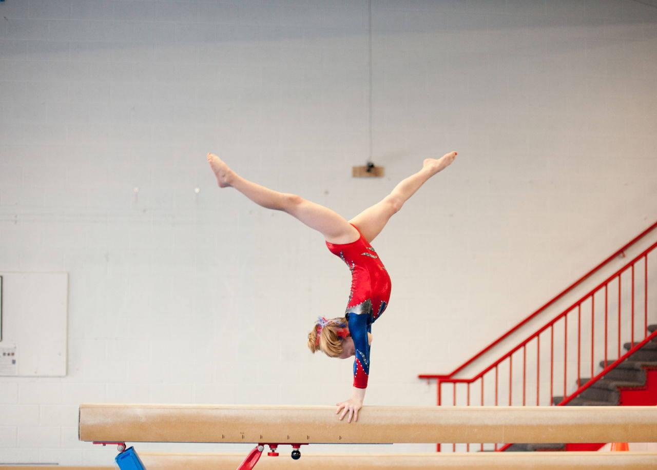 Young Gymnast In Handstand Split On Balance Beam Background