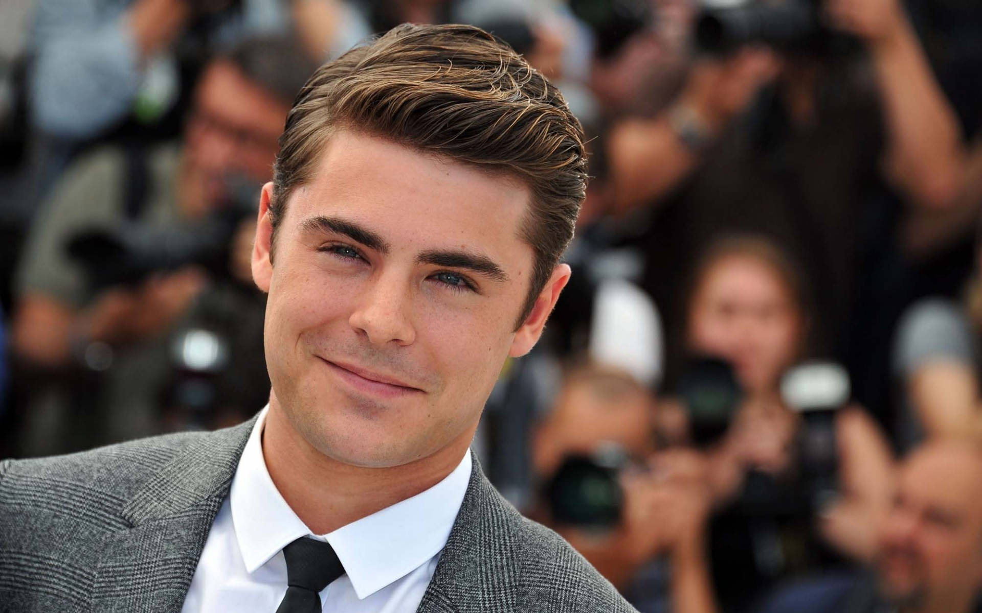 Zac Efron Grinning Cheekily In A Close-up Background