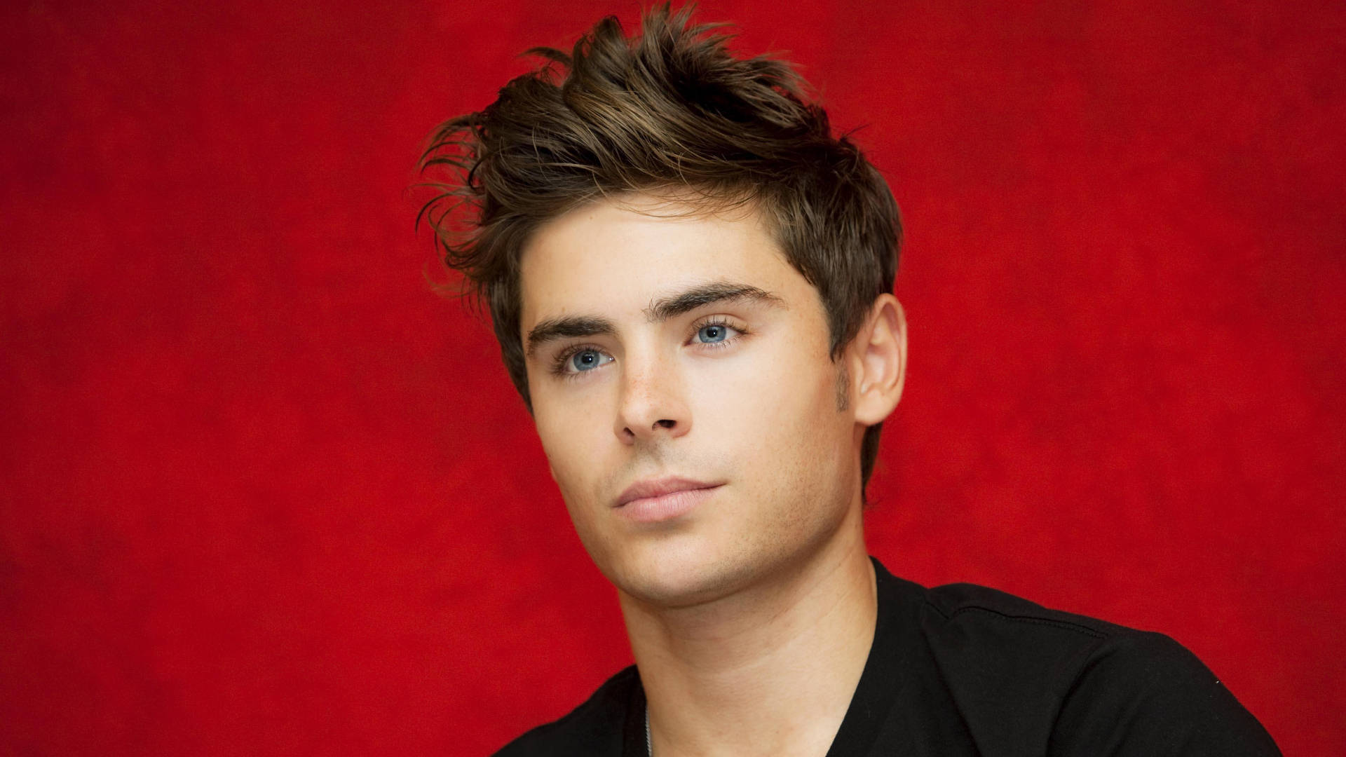 Zac Efron Looking Suave In A Red Backdrop Background