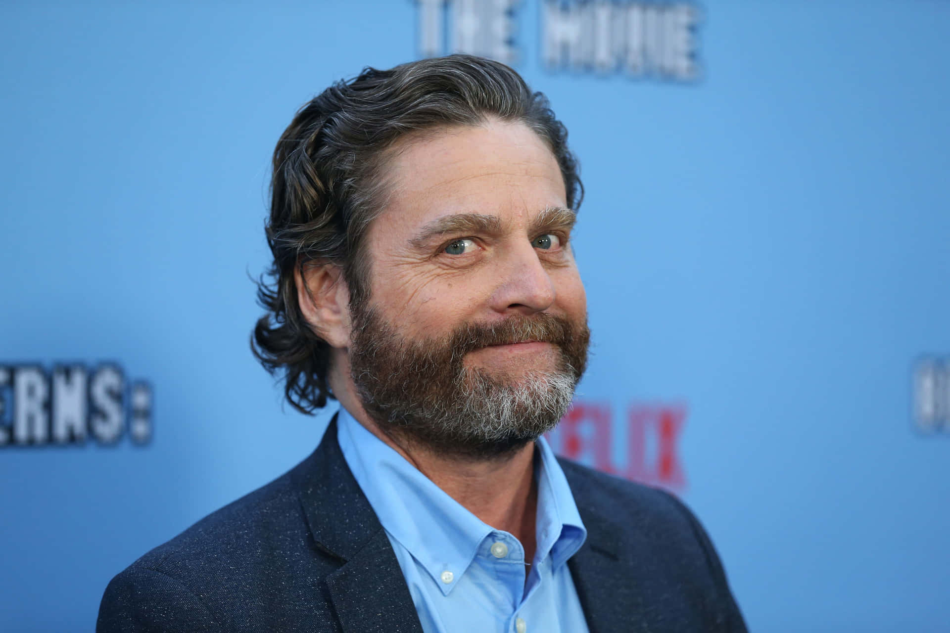 Zach Galifianakis Looking Pensive In A White Shirt And Denim Jacket Background